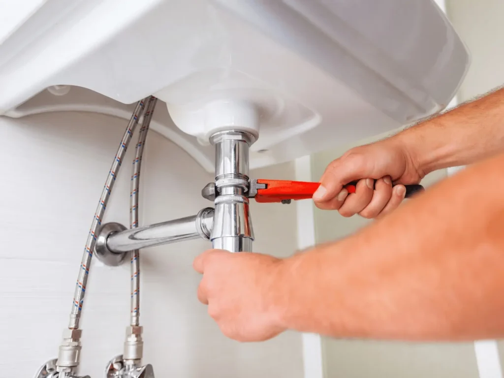 A plumber using a tool on pipes of a bathroom sink